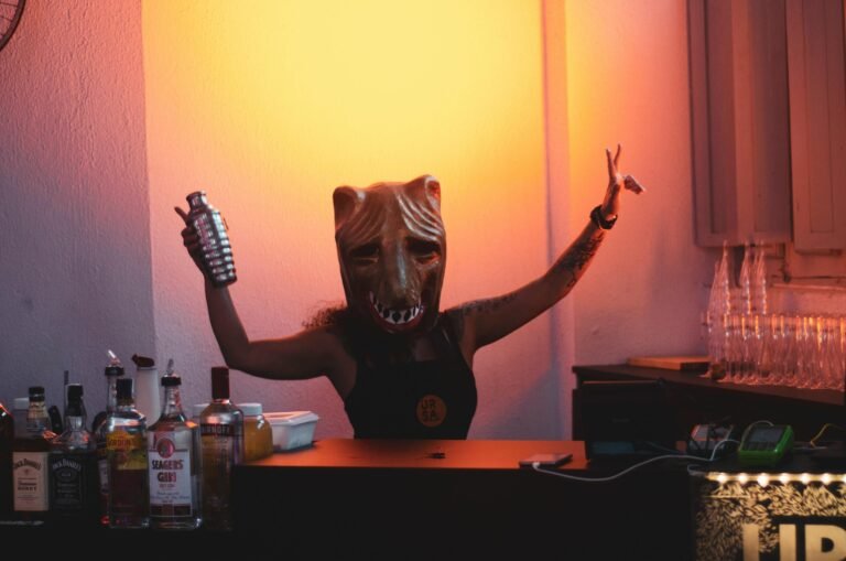 A bartender in a mask mixes drinks at an indoor party with a warm glow.