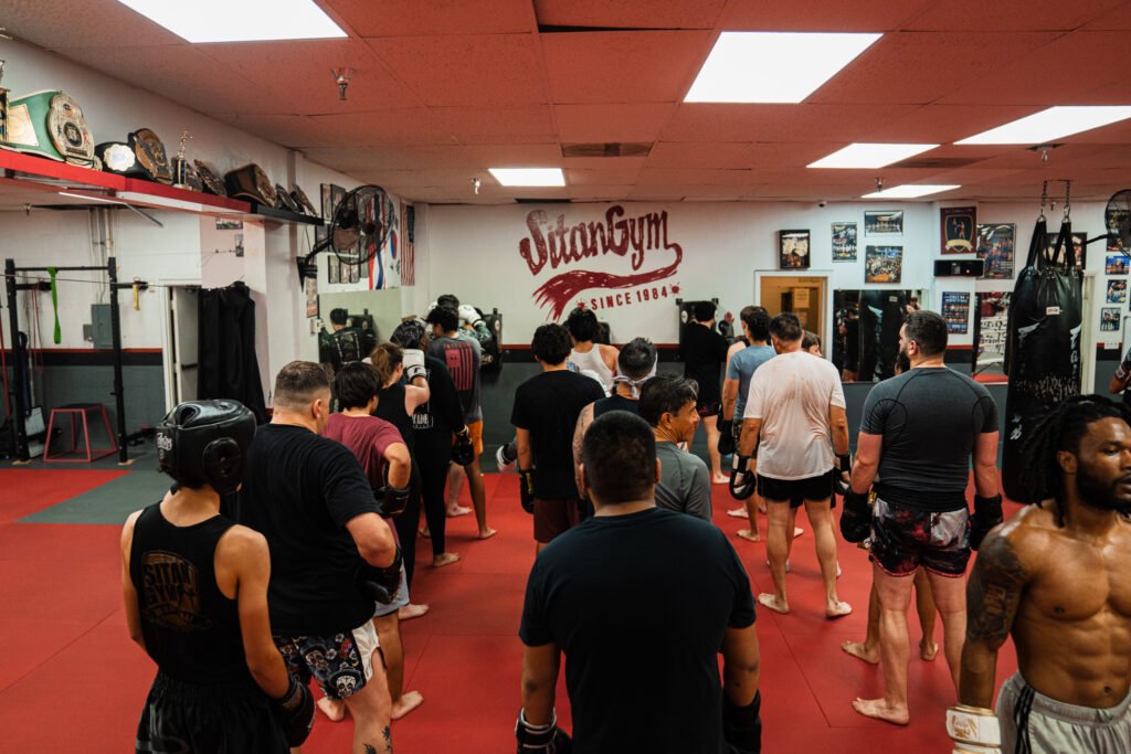 Three lines of students waiting for their turn at the wall bag. Sitan Gym logo is on the wall.