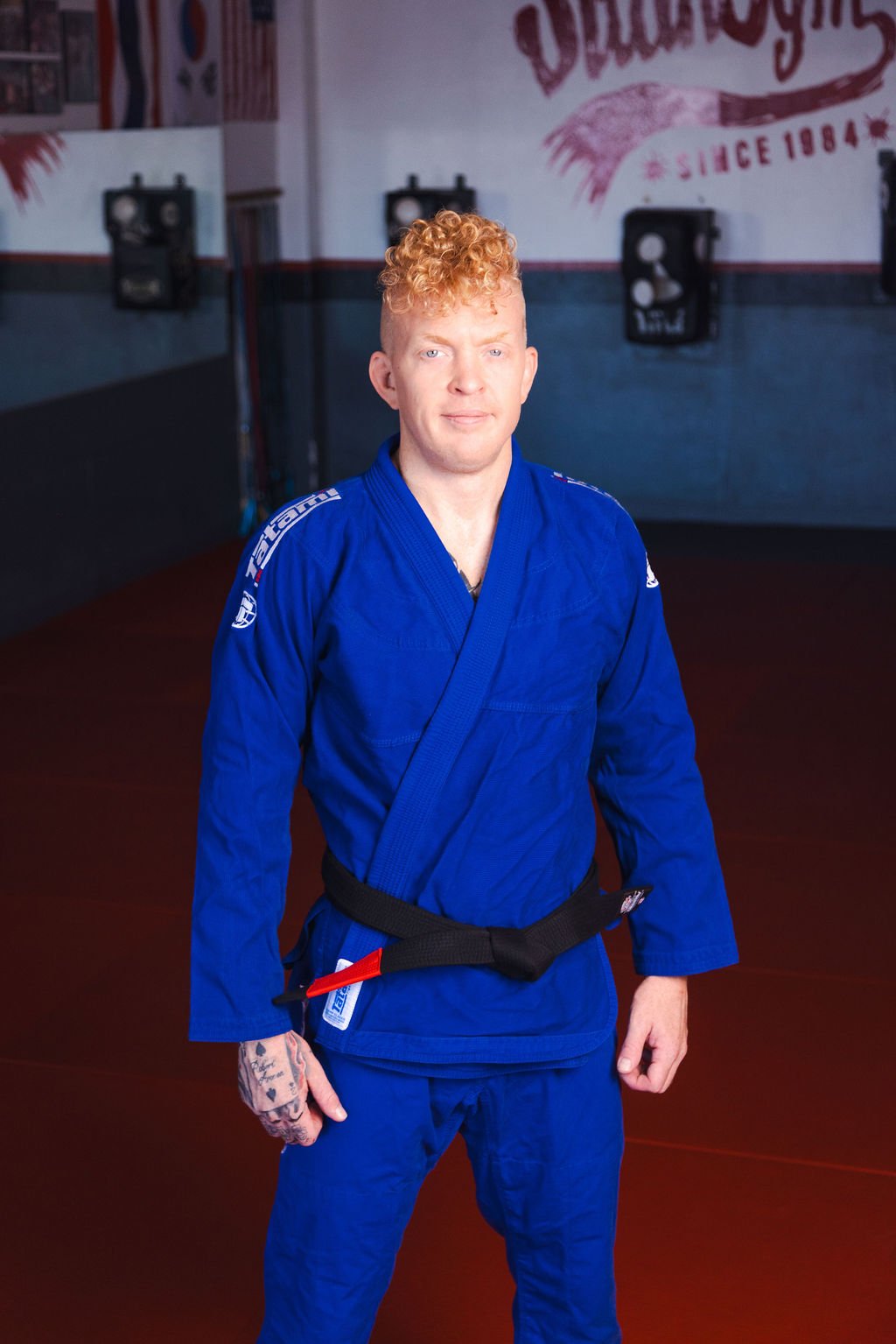 Man with a BJJ Blackbelt standing wearing a blue BJJ Gi